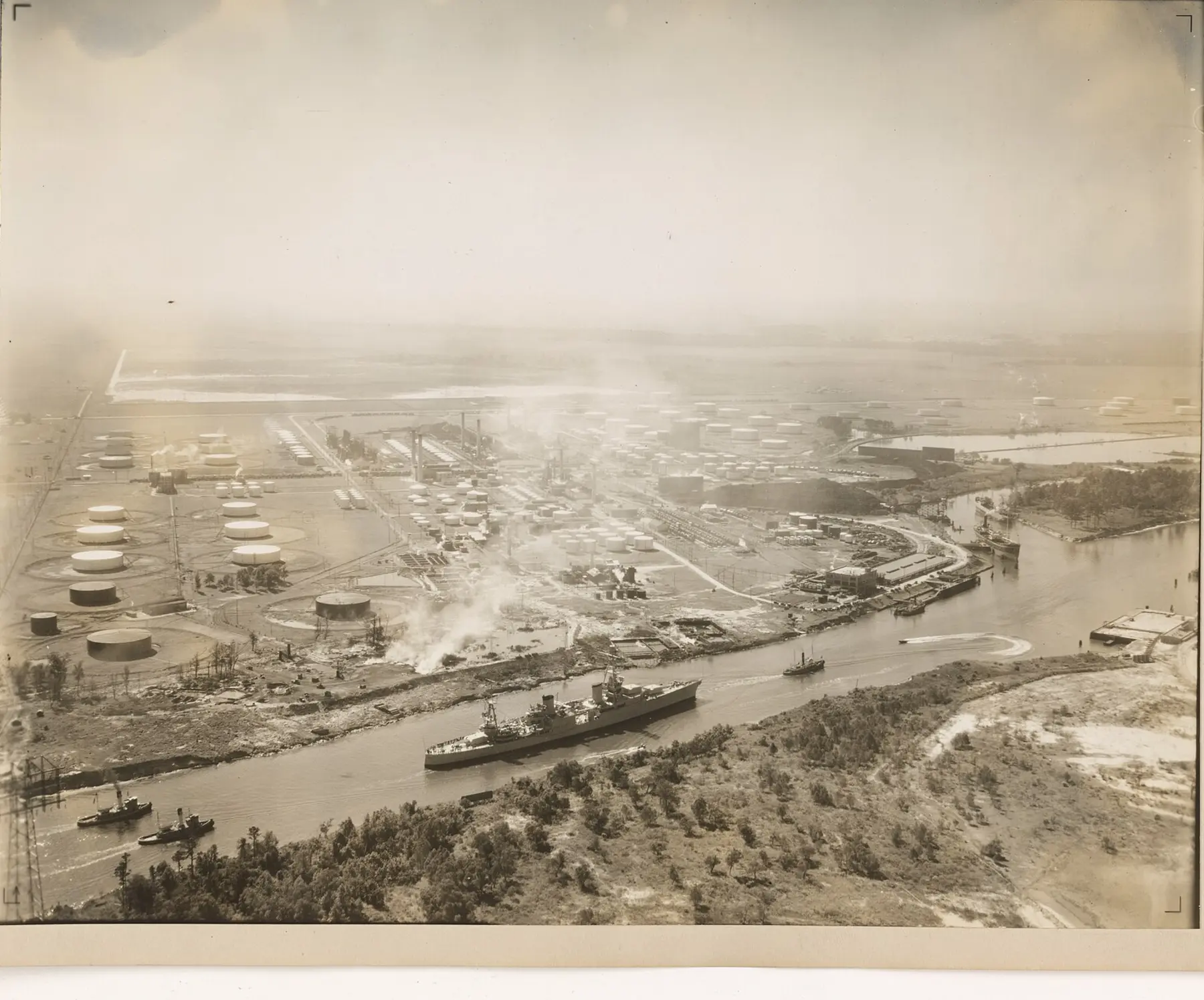 Historical aerial photograph of an industrial waterfront with storage tanks along a ship channel.
